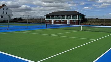 Blue and green outdoor tennis court with building in background